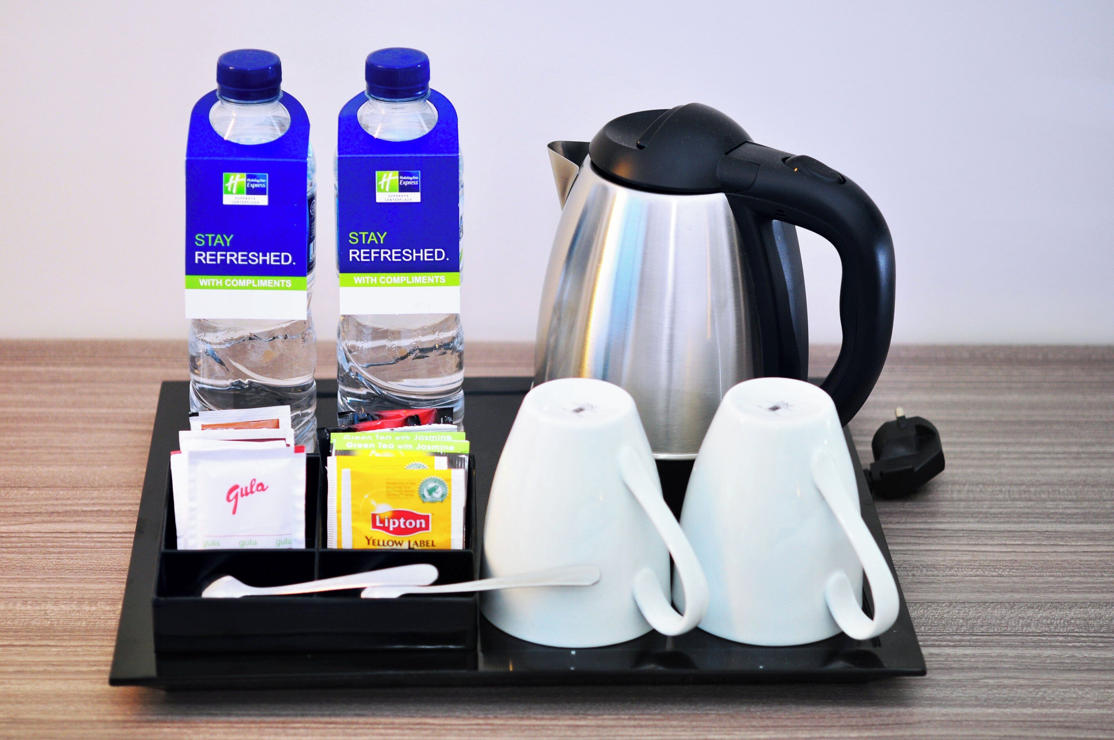 Una bandeja con dos botellas de agua, una tetera, dos tazas blancas, una bolsita de té y un paquete de té Lipton.