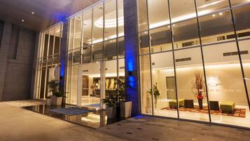 A modern hotel lobby with glass walls, a reception desk, seating area, and potted plants.
