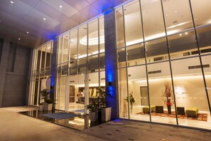 A modern hotel lobby with glass walls, a reception desk, seating area, and potted plants.