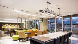 En moderne hotellobby med et langt spisebord, behagelige siddepladser og store vinduer med udsigt over byen.
