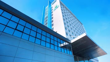 A modern hotel building with a prominent glass facade and a clear blue sky in the background.