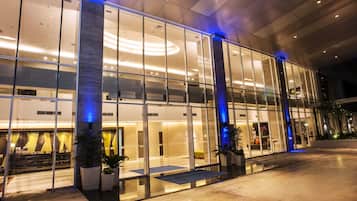 A modern hotel with a glass facade, large windows, and a well-lit interior.