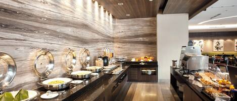 A buffet area with various food stations, a coffee machine, and a seating area with tables and chairs.