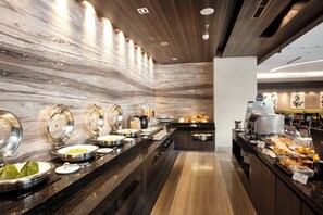 A buffet area with various food stations, a coffee machine, and a seating area with tables and chairs.