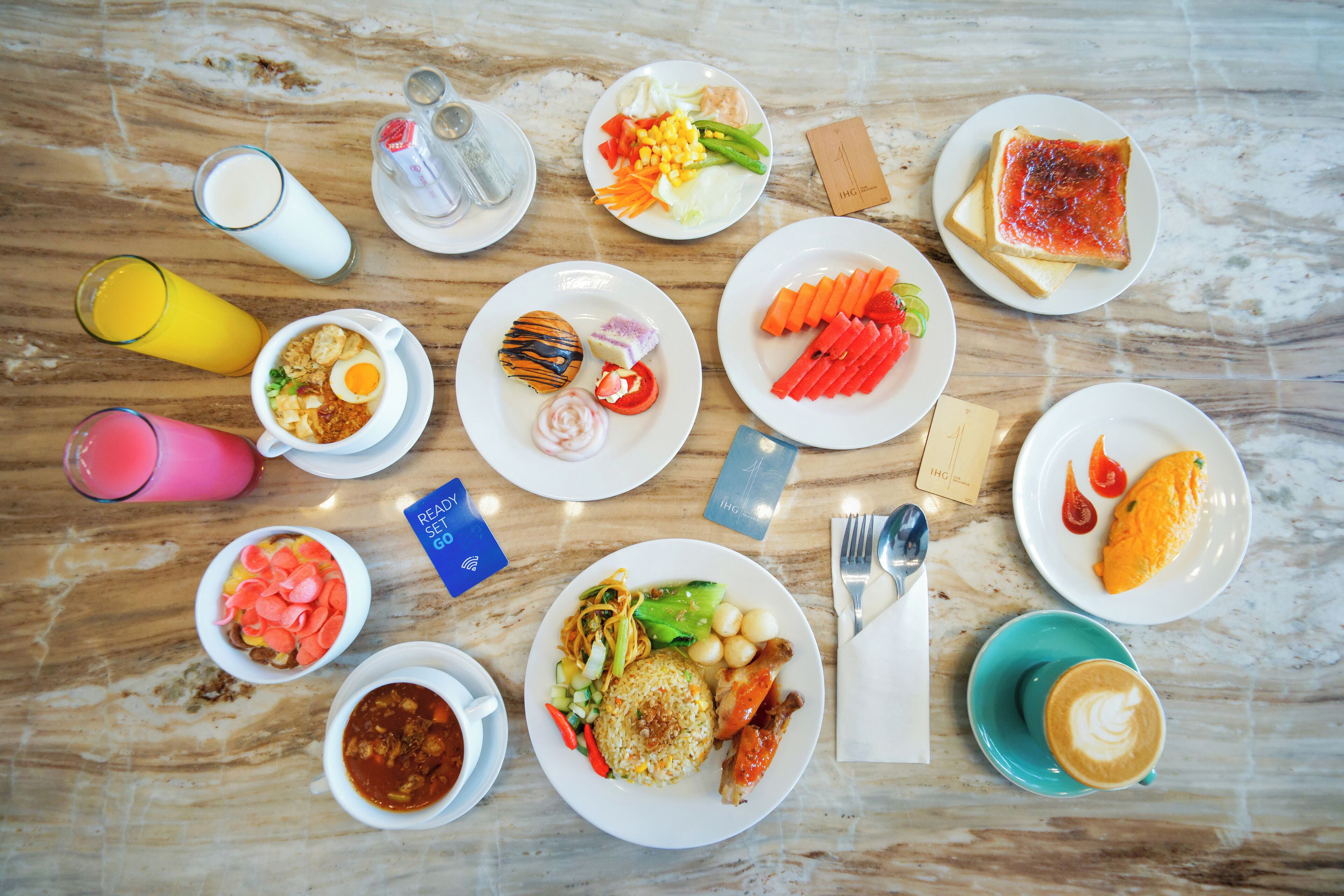 A variety of dishes and beverages on a marble table, including a plate with a fried egg, a bowl of soup, and a plate with sliced vegetables.