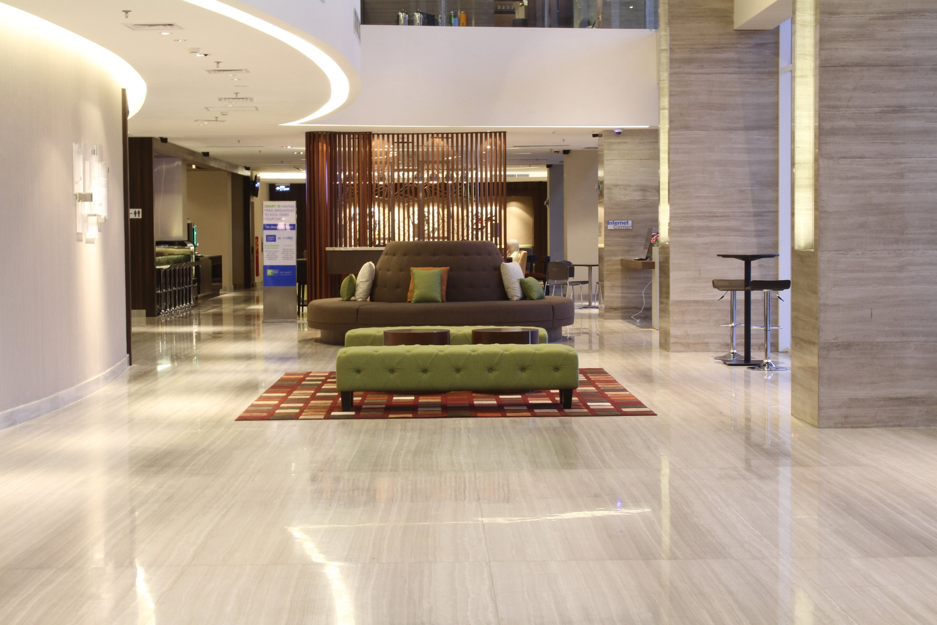 En moderne lobby med sofa og skammel, et receptionsområde og et skilt, der angiver gratis morgenmad.