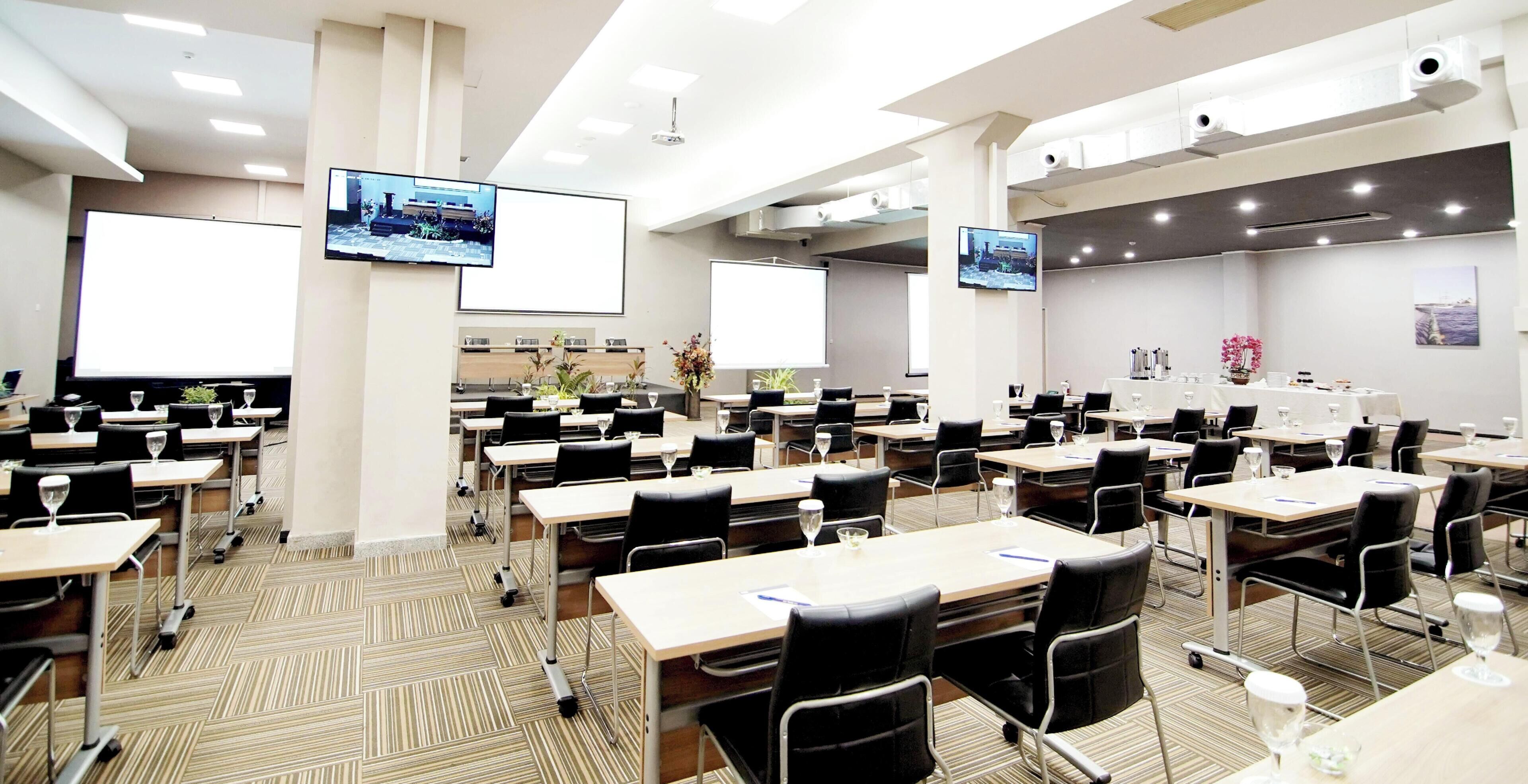 Un salón de conferencias con varias mesas, sillas y pantallas para presentaciones.