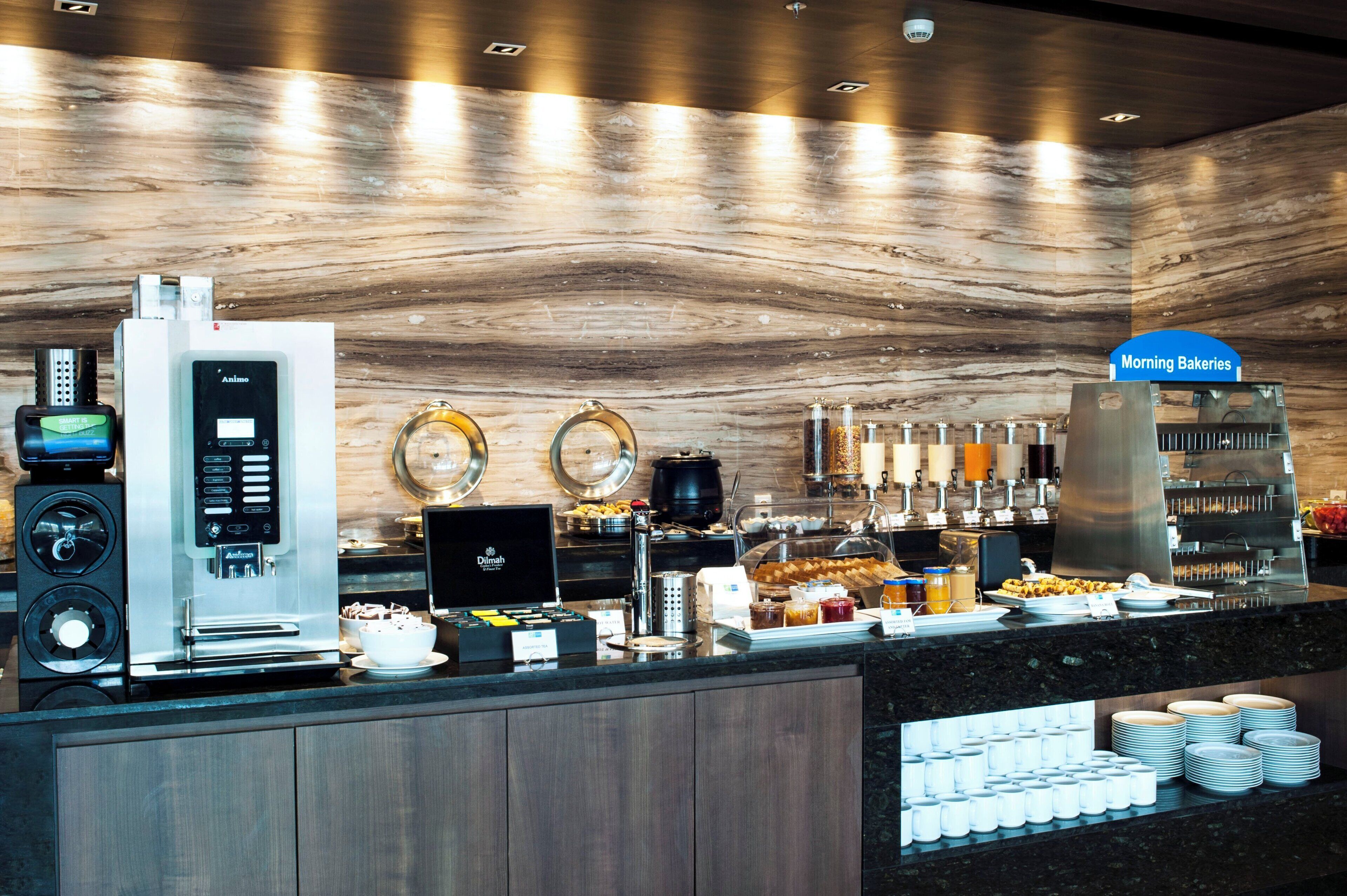 A breakfast buffet area with a coffee machine, tea station, and a variety of food options.
