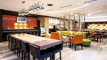 A hotel lobby with a reception desk, a long communal table, and several seating areas with chairs and sofas.