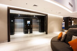 A modern hotel lobby with a marble floor, an elevator, and a seating area with a sofa and cushions.