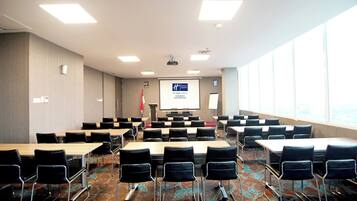 Una sala de conferències amb taules i cadires, una pantalla de projector i una bandera.