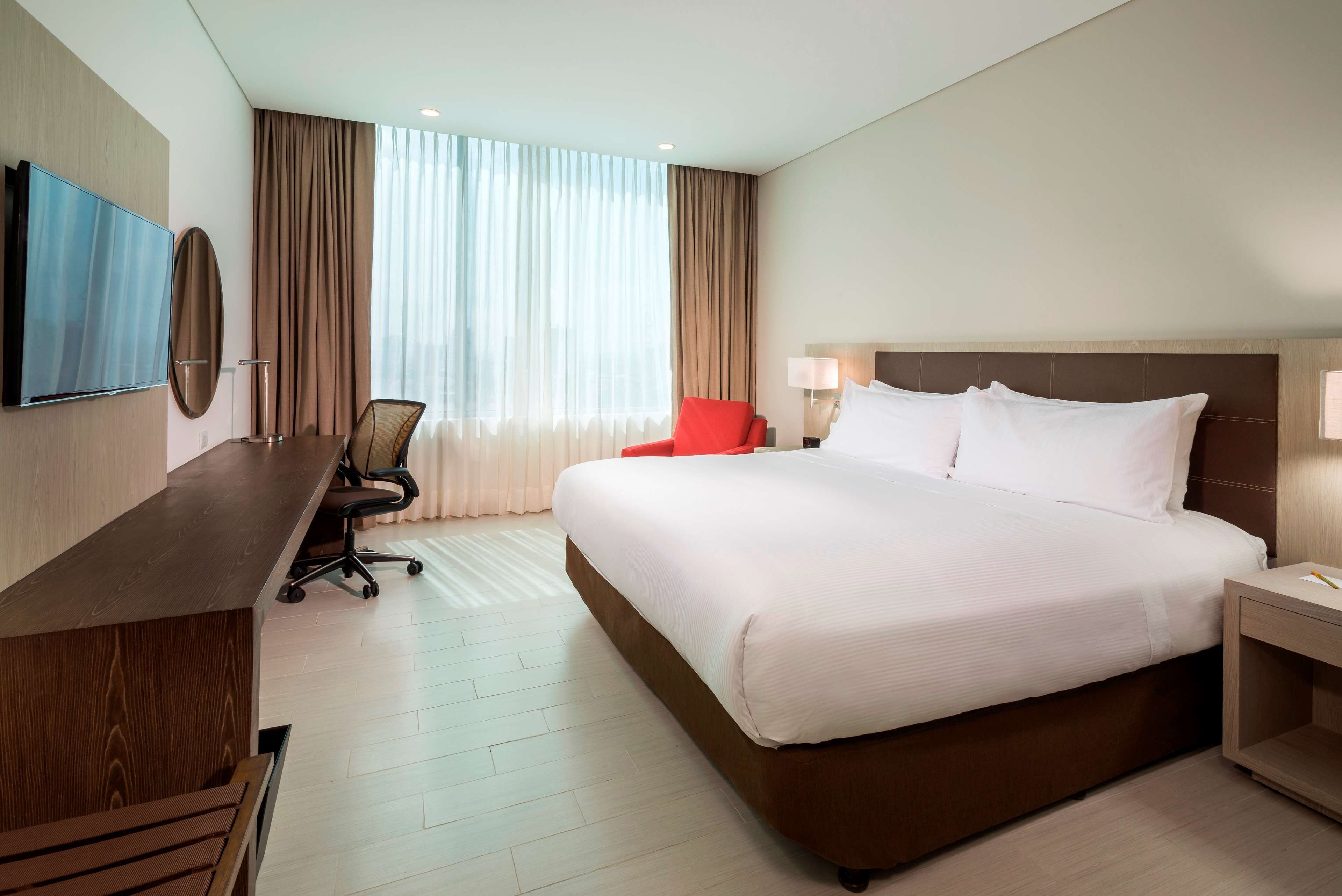 Habitación de hotel con una cama grande, un escritorio con silla, televisor y ventana con cortinas.