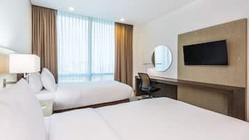 Habitación de hotel con dos camas, un escritorio, una silla, un televisor, un espejo y una ventana con cortinas.