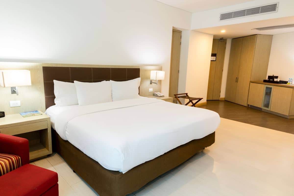 A hotel room with a large bed, a nightstand, a red chair, and a wardrobe.