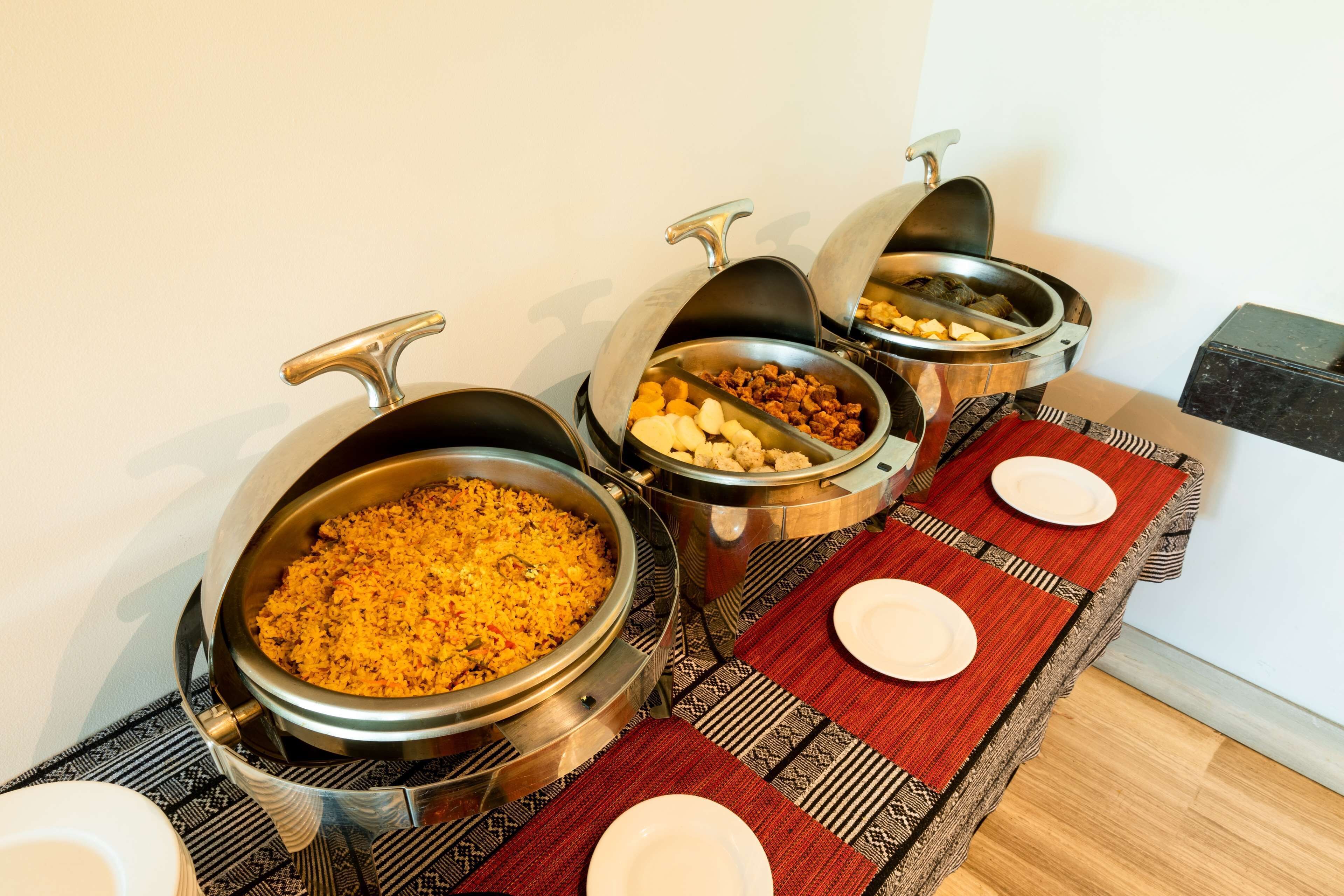 A buffet setup with various food items in metal containers, a table with red placemats and white plates, and a black marble countertop.