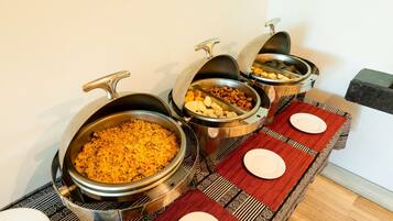 A buffet setup with various food items in metal containers, a table with red placemats and white plates, and a black marble countertop.