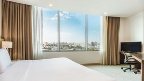 A hotel room with a large bed, a desk with a chair, a television, and a city view through large windows. - Hilton Garden Inn Barranquilla (Barranquilla)