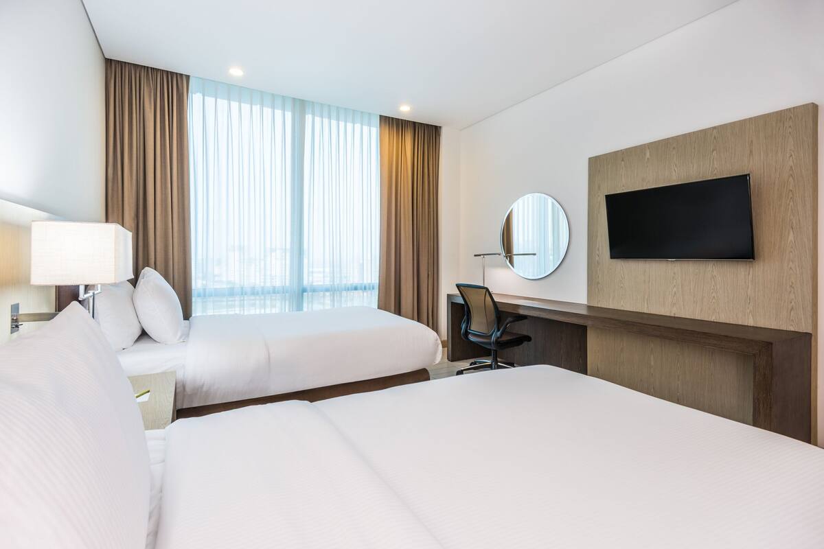 A hotel room with two beds, a desk, a chair, a TV, and a window with curtains.