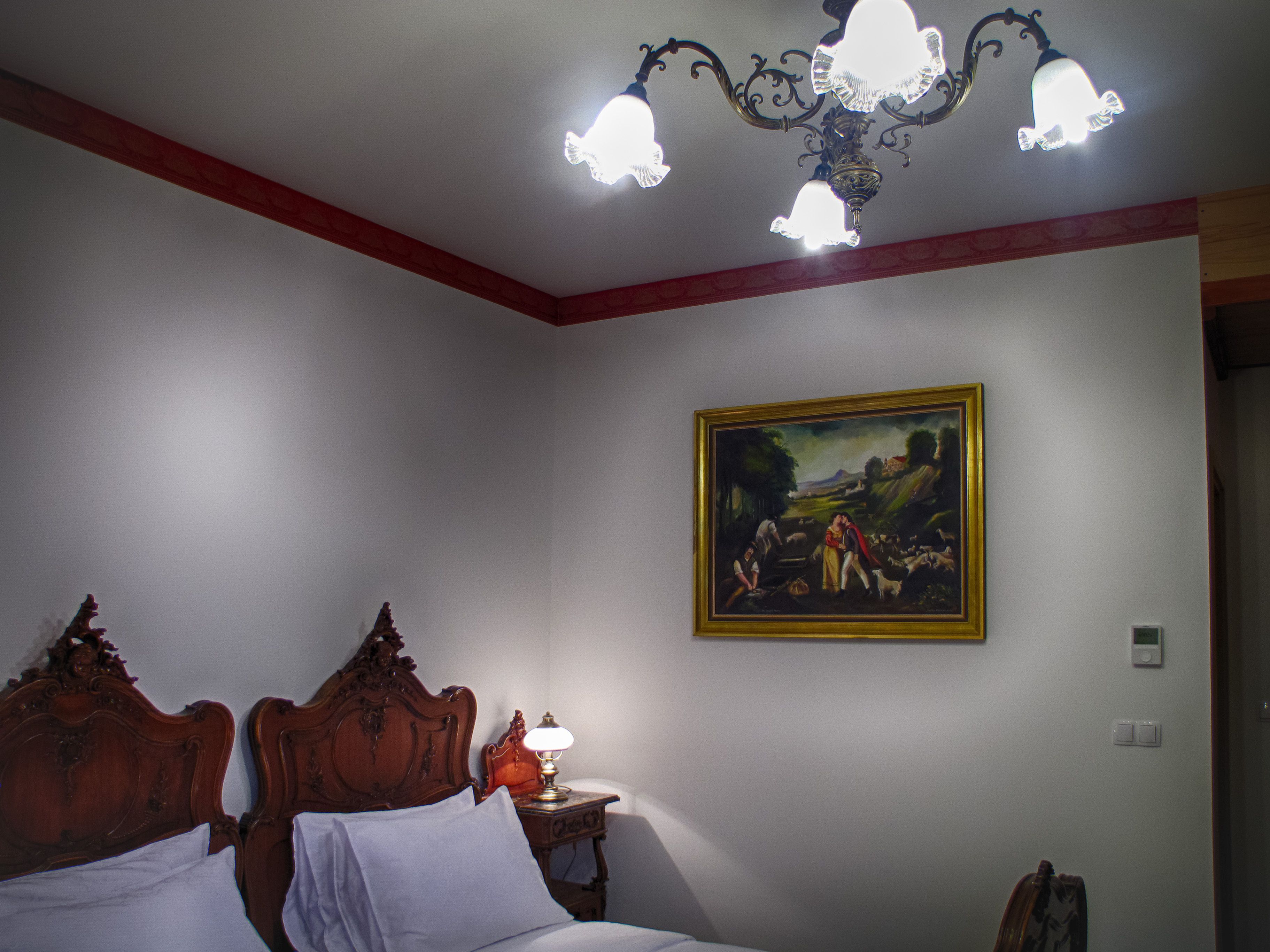 A bedroom with a wooden bed, a nightstand, a lamp, and a painting on the wall.
