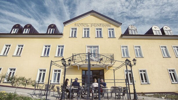 A yellow building with the sign "HOTEL PANTIJAR" and a balcony with tables and chairs.