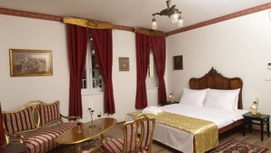 Habitación de hotel con una cama grande, un sofá, una mesa de comedor y una araña.