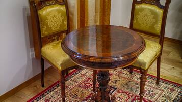 Uma mesa de madeira redonda com tampo de vidro, acompanhada por duas cadeiras elaboradas com estofamento dourado.