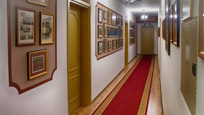 Un pasillo con cuadros enmarcados en las paredes, puertas de madera y una alfombra roja.