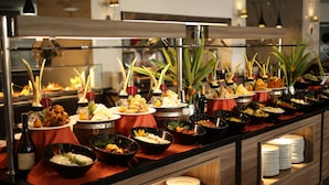 A buffet with various dishes and drinks, including bowls of food, bottles of wine, and decorative plants.