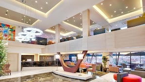 A modern hotel lobby with a marble floor, a reception desk, and a seating area with colorful chairs.