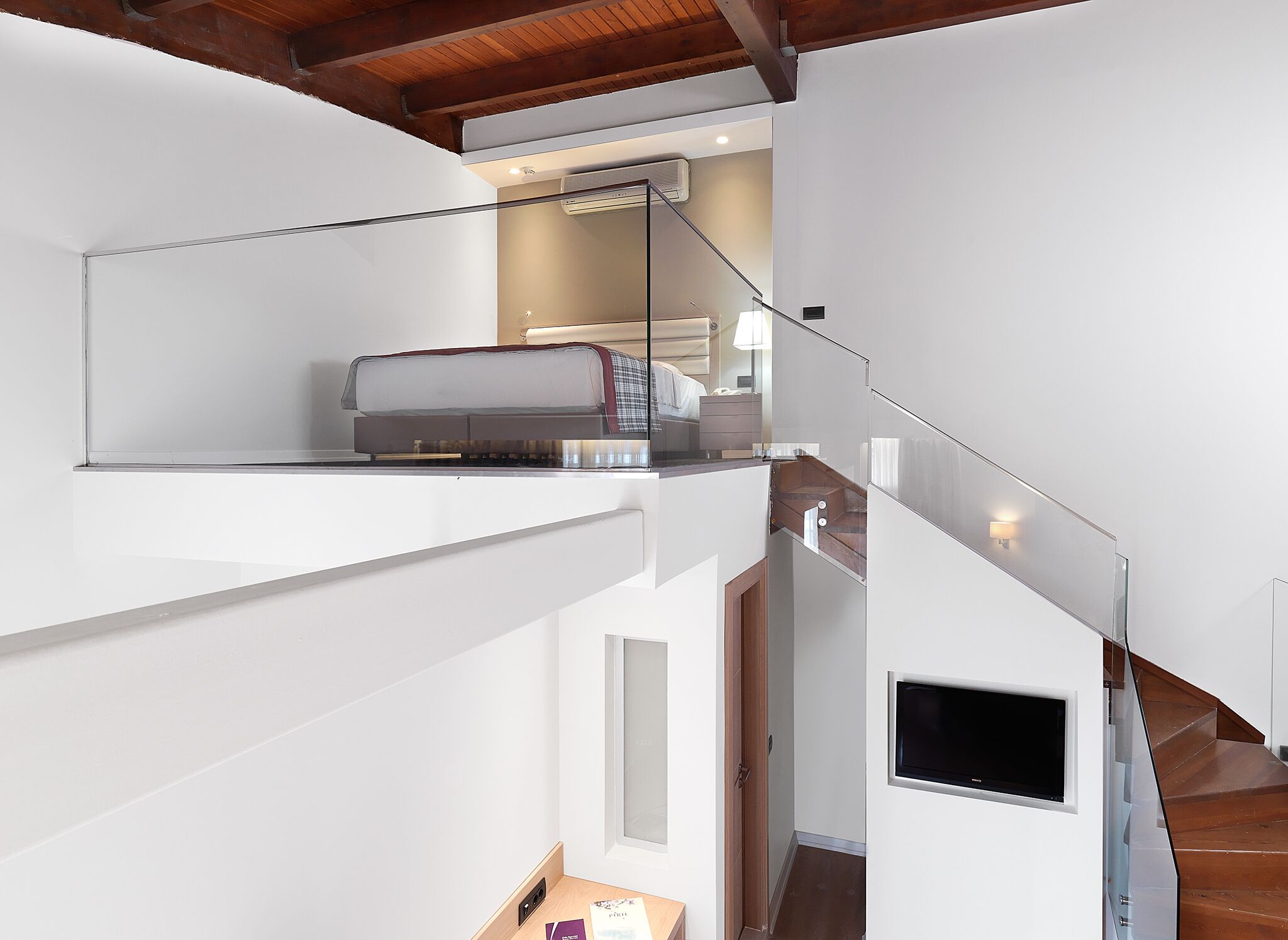 A modern interior with a staircase, a book on a shelf, and a TV mounted on the wall.
