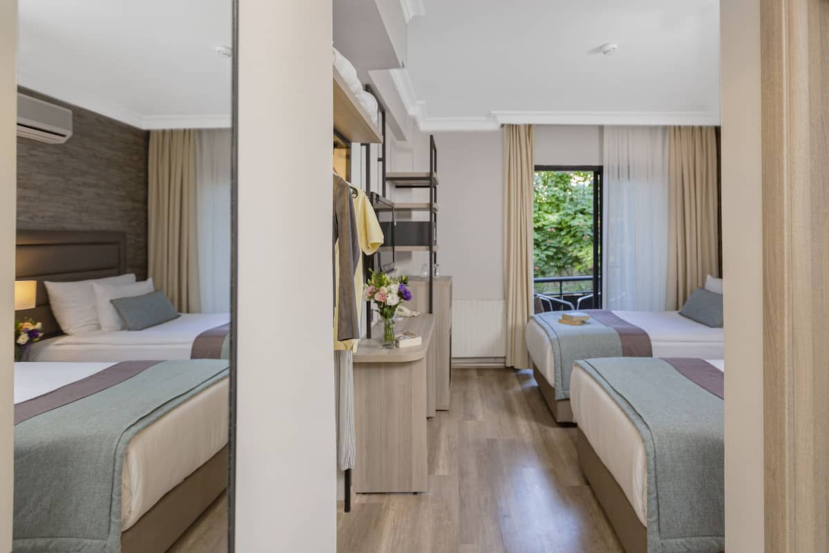 A hotel room with two beds, a small desk with a vase of flowers, and a view of greenery outside.