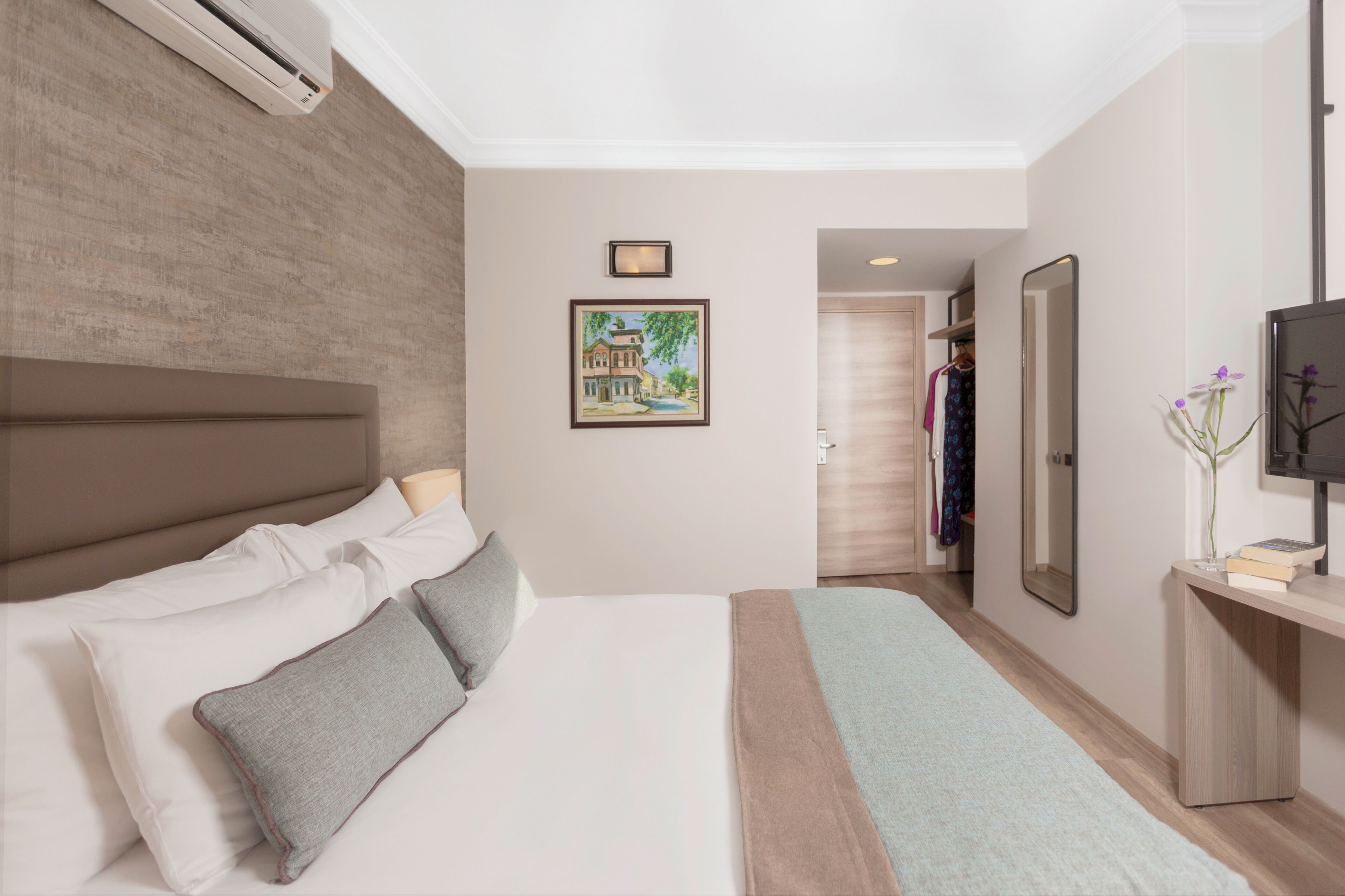 A hotel room with a large bed, a bedside table, a mirror, and a painting on the wall.