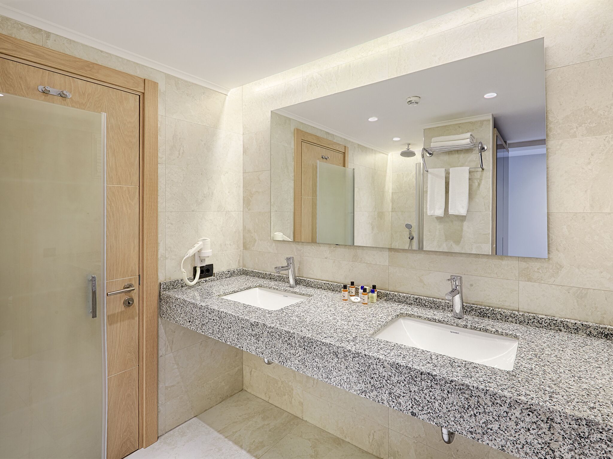 Une salle de bain moderne avec deux lavabos, un grand miroir et une douche.