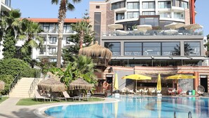 A hotel with a swimming pool, outdoor seating, and a multi-story building with balconies.