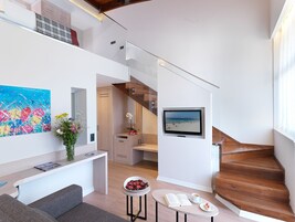 Un interior moderno con una escalera, un televisor de pantalla plana, un comedor con mesa y sillas, un sofá y un cuadro en la pared.
