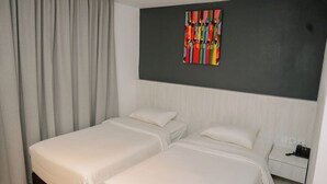 Une chambre d’hôtel avec deux lits, une table de chevet avec un téléphone et une peinture abstraite aux couleurs vives accrochée au mur.