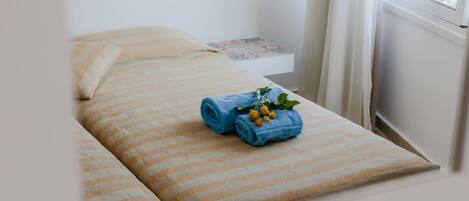 A neatly made bed with striped bedding and a rolled blue towel with a flower.
