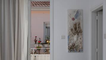 Un interno moderno con una panca bianca, un elemento decorativo a parete e vista su un balcone con piante e fiori.