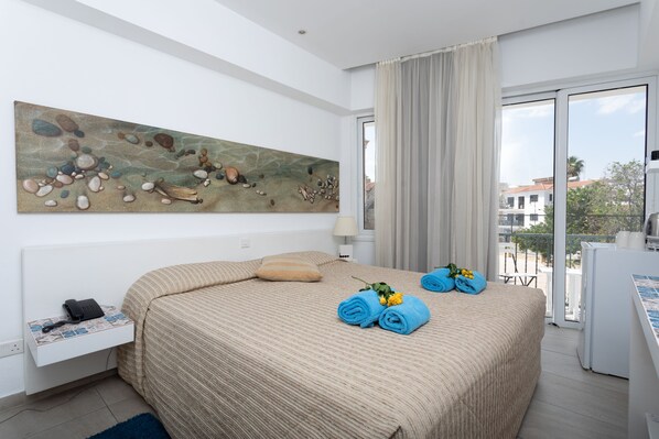 A hotel room with a large bed, a painting on the wall, a window with curtains, and a balcony with a view.