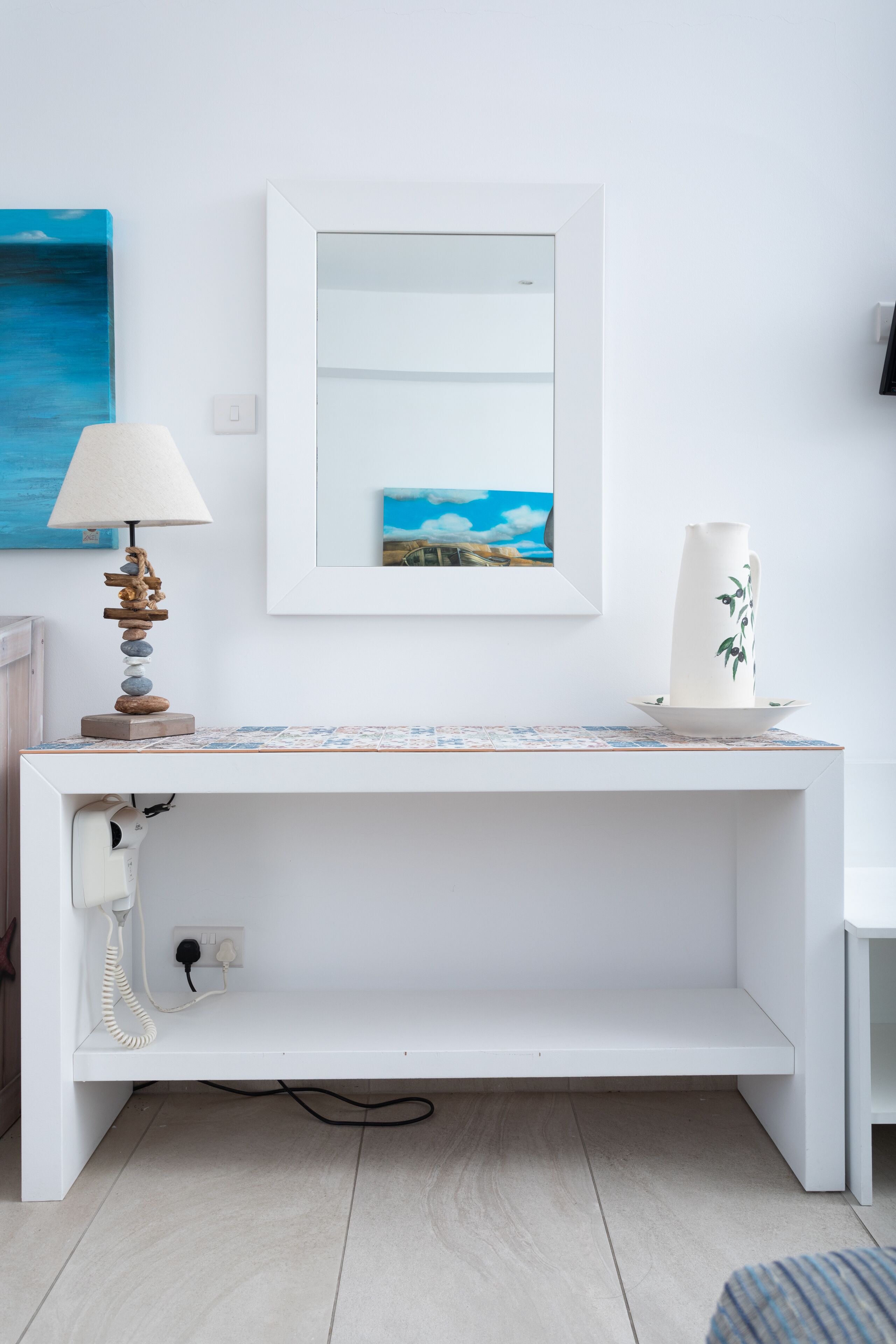 A white console table with a lamp, a vase, and a framed picture on the wall above.