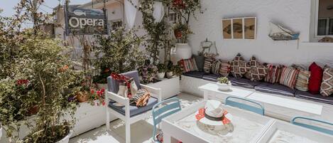An outdoor seating area with white furniture, potted plants, and a sign reading "Opera".