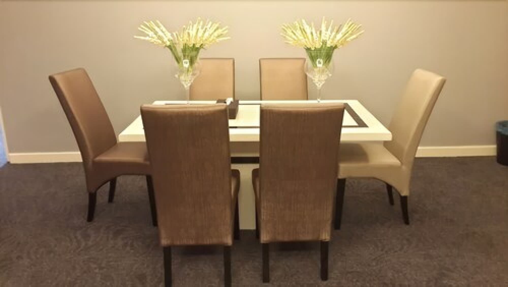 Un comedor con una mesa rectangular, cuatro sillas y dos jarrones con flores.