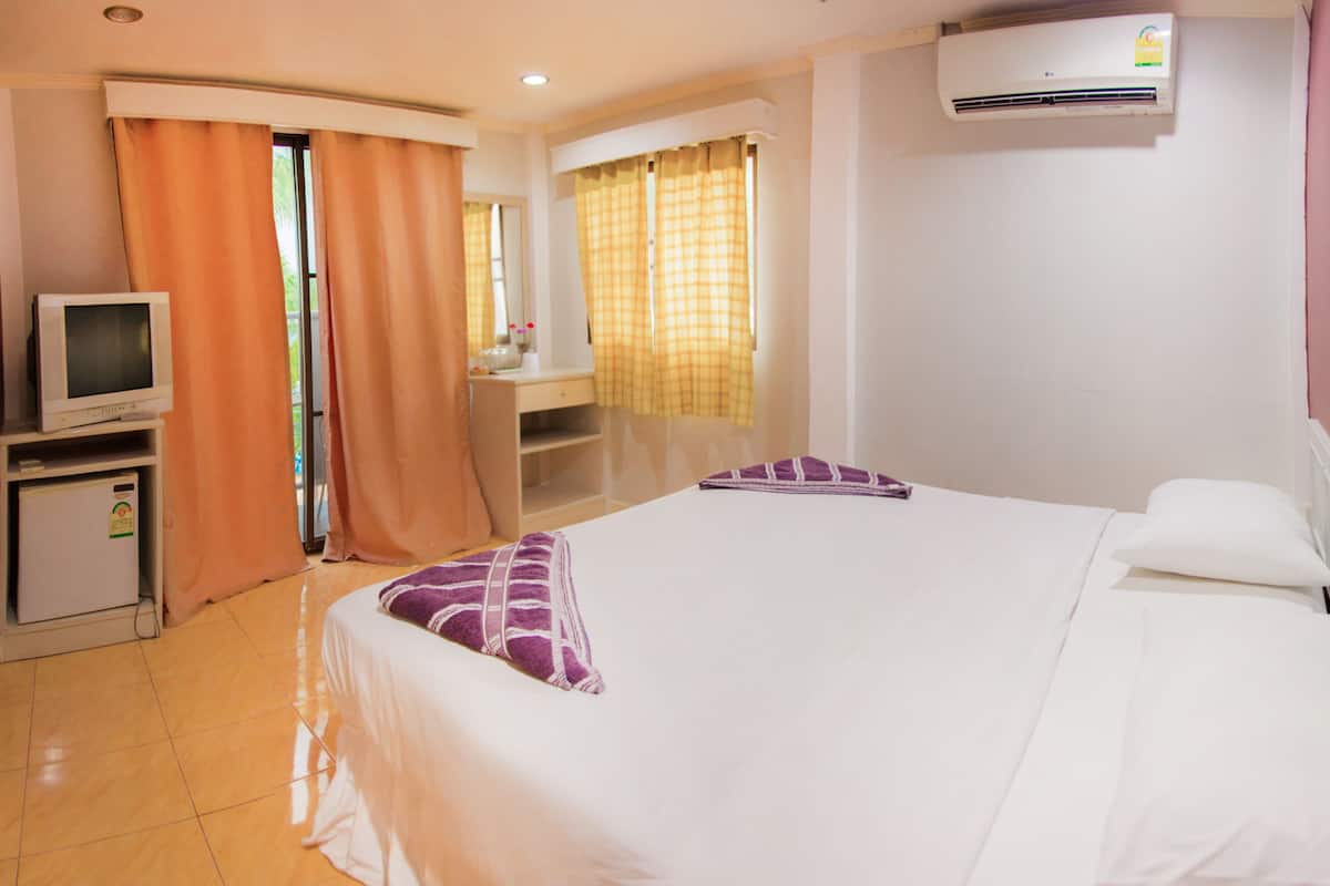 Una habitación de hotel con cama, escritorio, televisor y aire acondicionado.