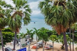 A beach view with palm trees, a boat in the water, and a building with a sign. - G.I Lodge (Pattaya)