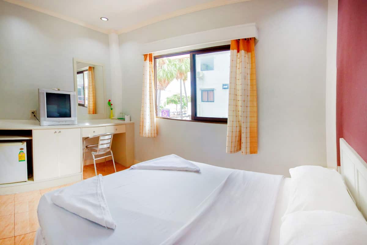 Habitación de hotel con cama, escritorio con computadora, una silla y ventana con cortinas.