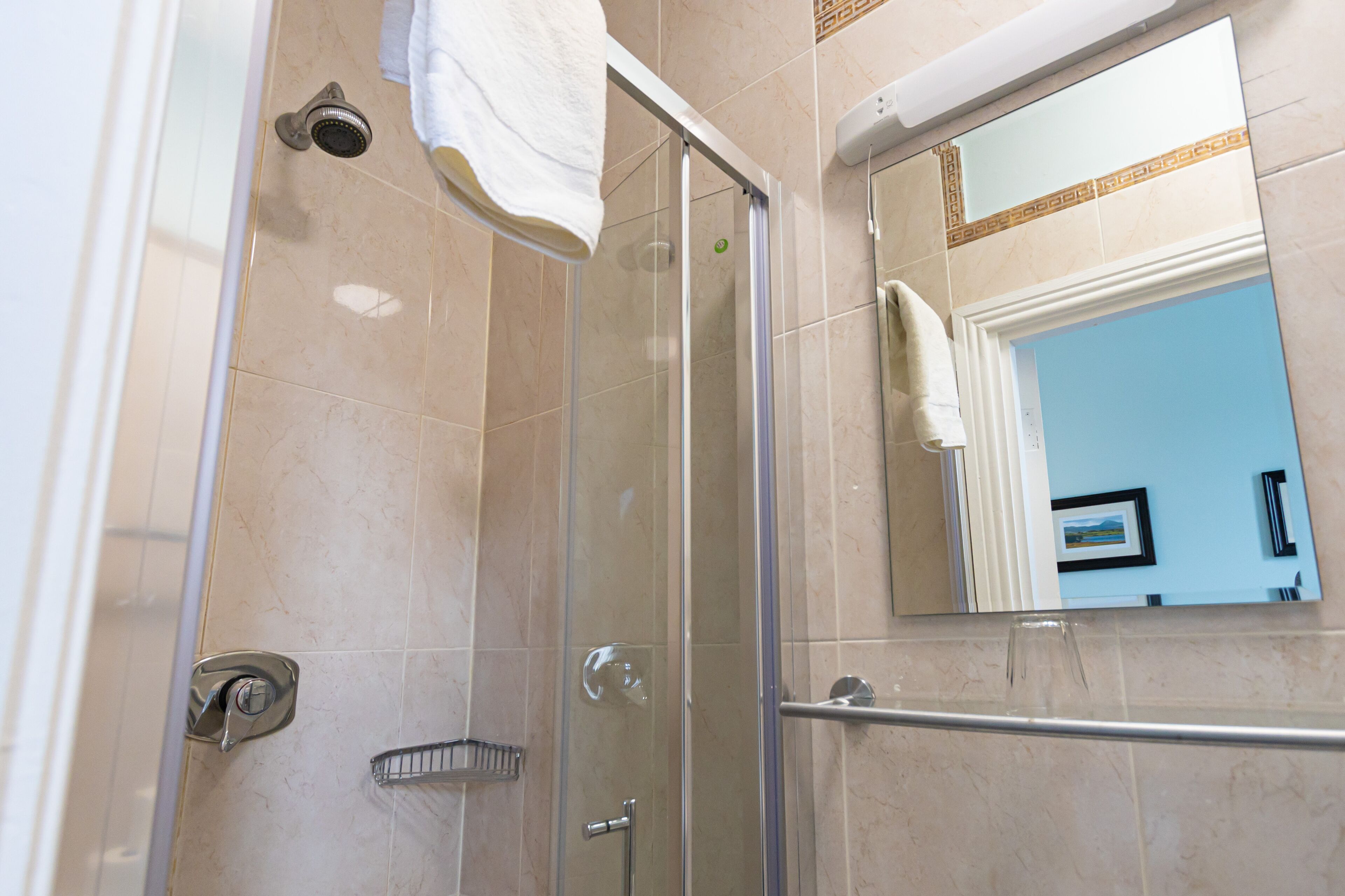 A glass-enclosed shower stall with a towel hanging on the door, a showerhead, and a handrail.