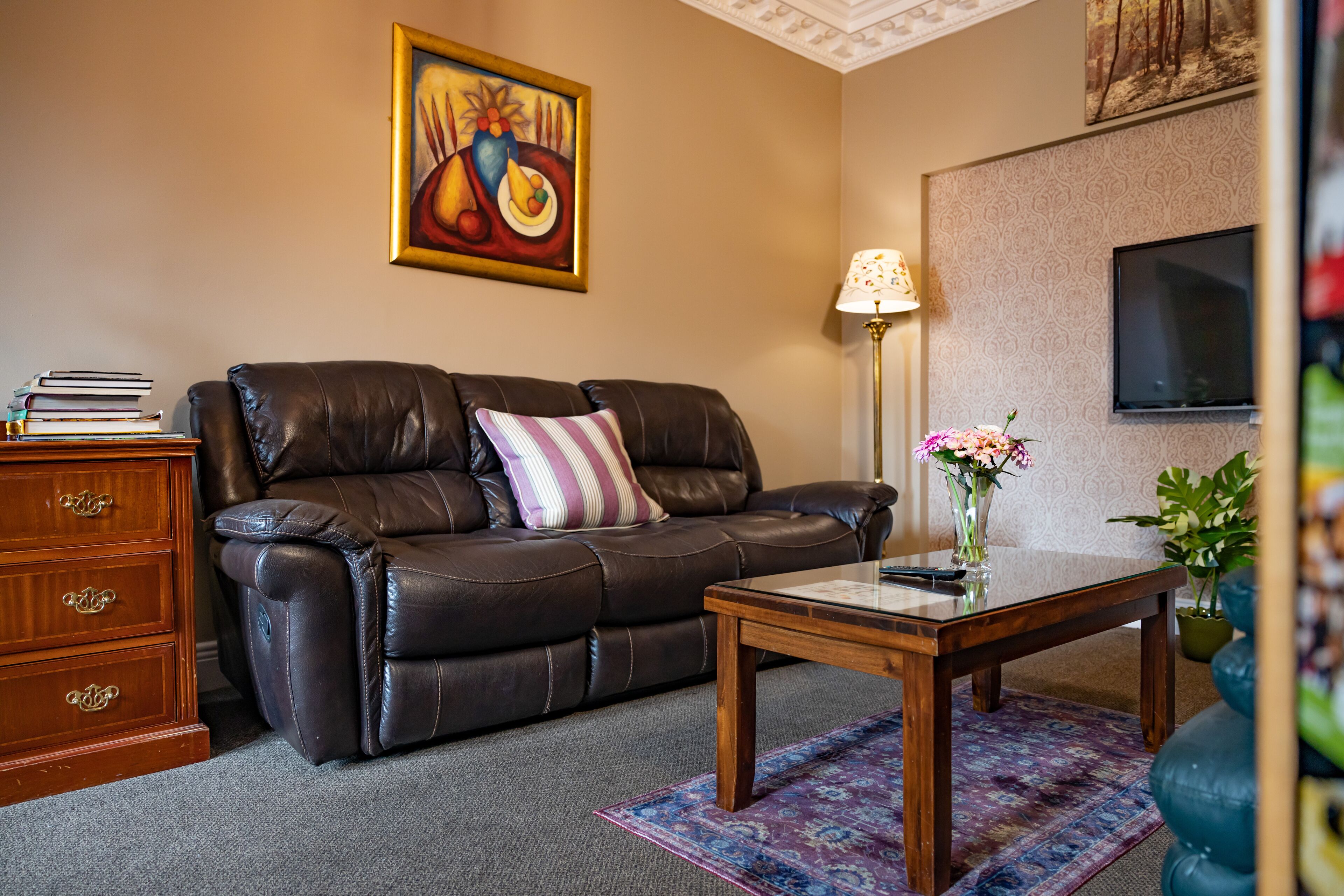 A living room with a leather sofa, a wooden coffee table, a lamp, and a painting on the wall.