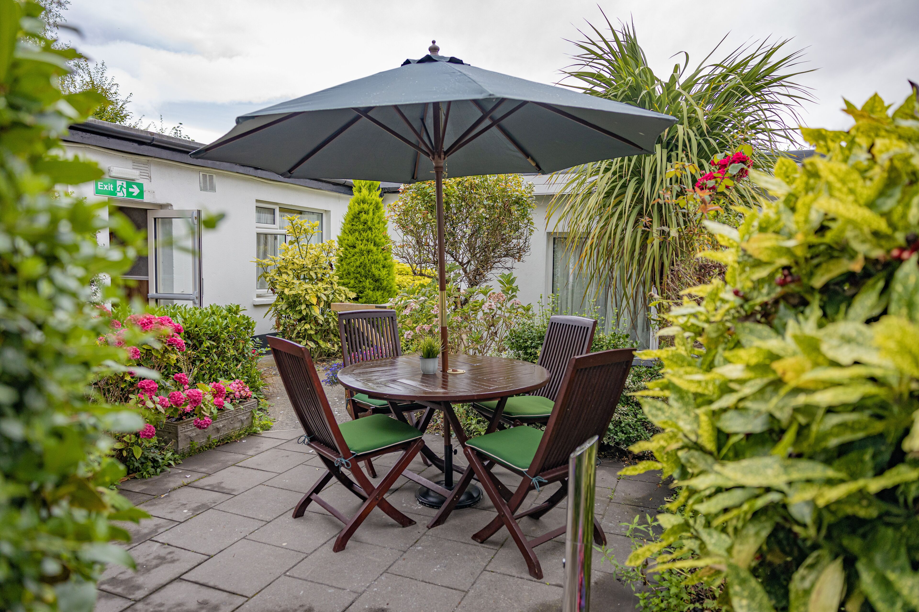 A patio with a round table and four chairs, an umbrella, and a sign indicating an exit.