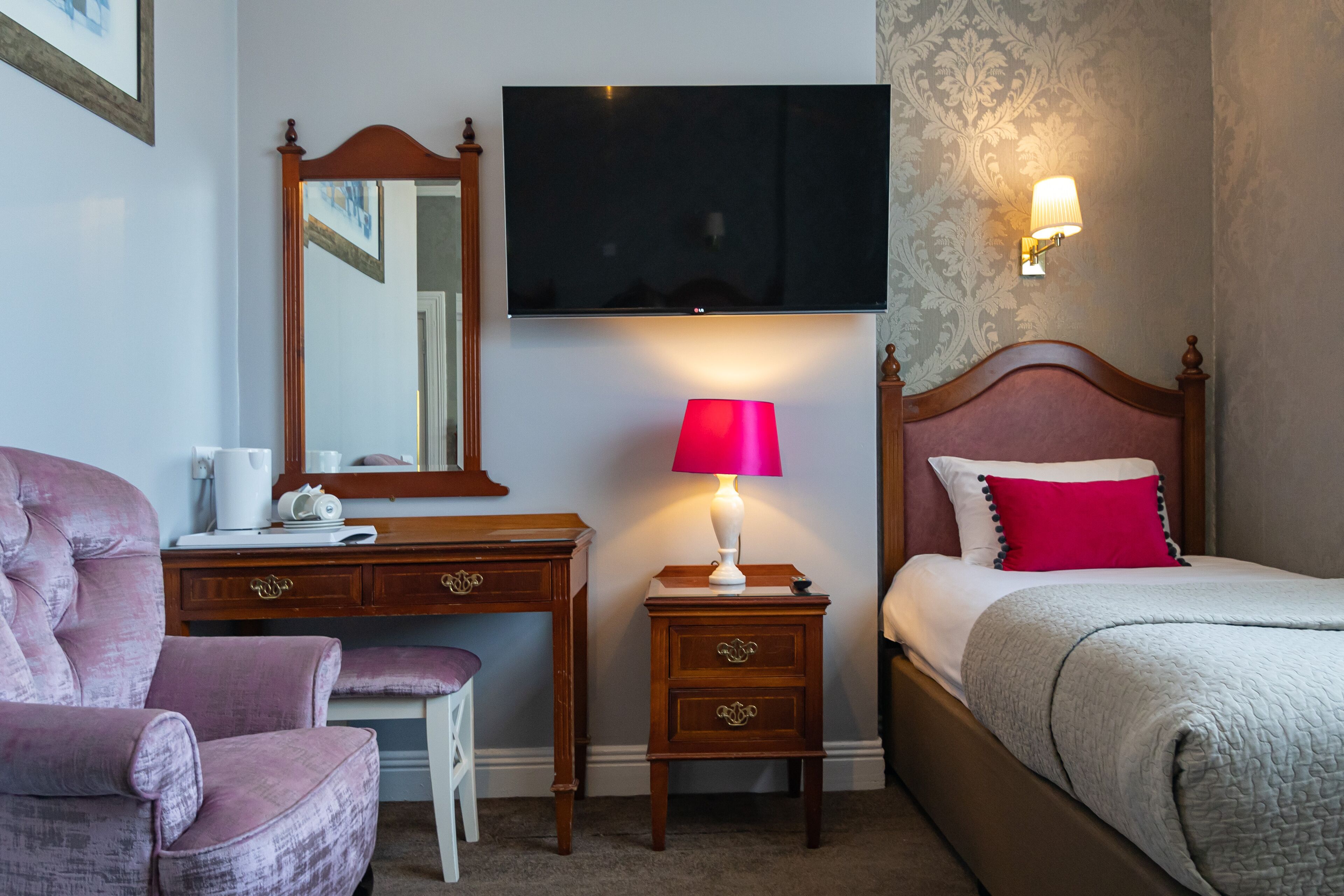 Una habitación de hotel con una cama, un escritorio con una silla, un televisor y una mesita de noche con una lámpara.