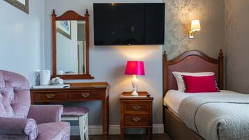 A hotel room with a bed, a desk with a chair, a television, and a nightstand with a lamp.